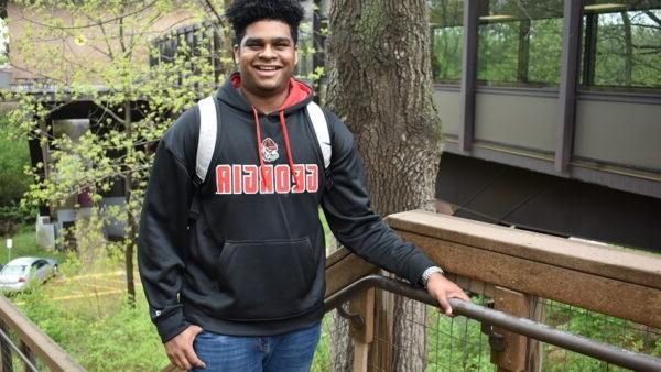 smiling male college student standing at the top of a staircase on campus with trees in the background